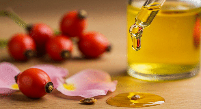 Una goccia di olio di rosa mosqueta che cade da un contagocce con petali di rosa sullo sfondo, a simboleggiare il rimedio naturale per le macchie solari.