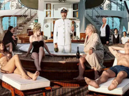 Il cast del film Triangle of Sadness posa sulla coperta di uno yacht di lusso. Al centro, il capitano interpretato da Woody Harrelson si trova in uniforme dentro una vasca idromassaggio, circondato dai ricchi passeggeri.