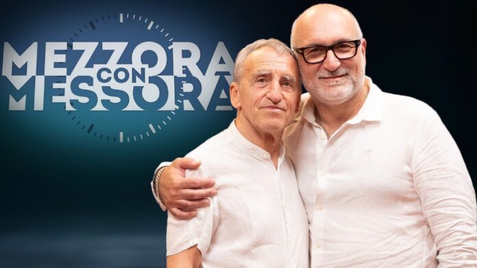 Mauro Scardovelli e Claudio Messora si abbracciano di fronte al logo della trasmissione 